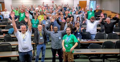 A picture of session attendees in a conference room with their hands raised up in the air.