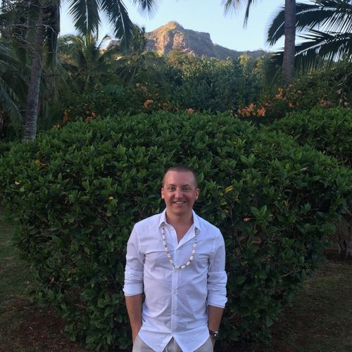 Adam smiling with palm trees and a tropical mountain range in the distance.
