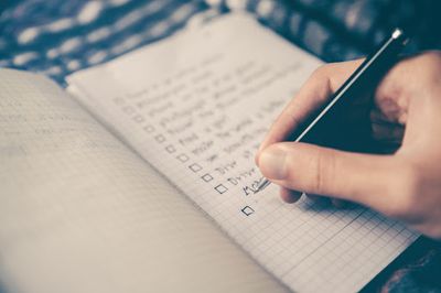 Hand with pen hovering over a checklist in a notepad