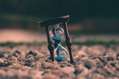 An hourglass with blue sand sitting on rocks.